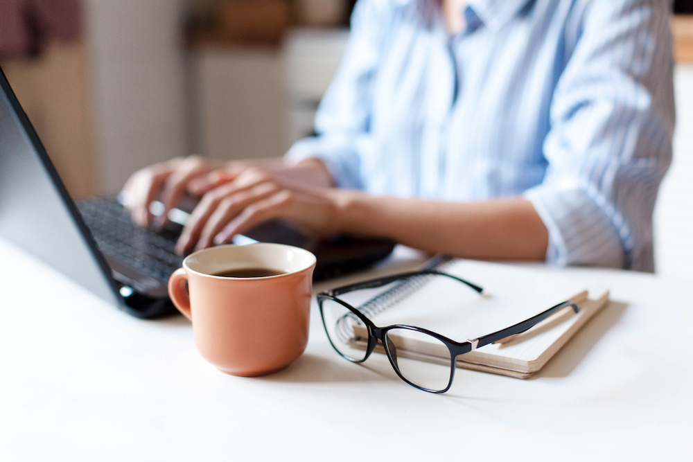 woman workplace in kitchen with laptop, cup of coffee, spectacles.