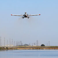 rice seeding plane flying over flooded field